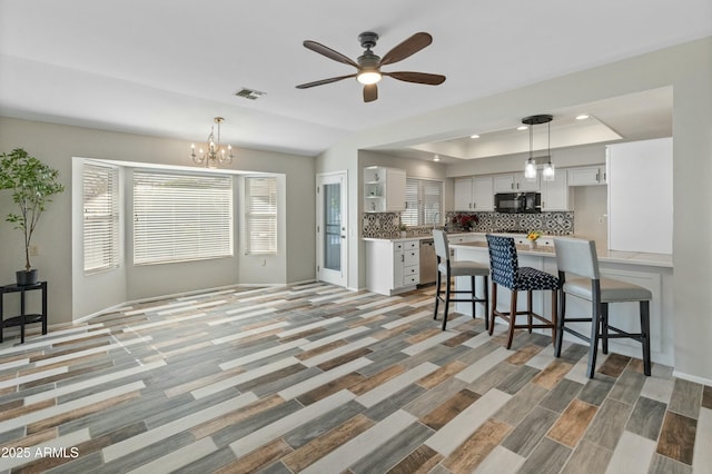 kitchen featuring ceiling fan with notable chandelier, pendant lighting, white cabinetry, tasteful backsplash, and a raised ceiling