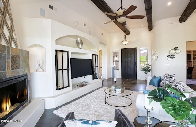 living room featuring beam ceiling, a tile fireplace, ceiling fan, and a high ceiling