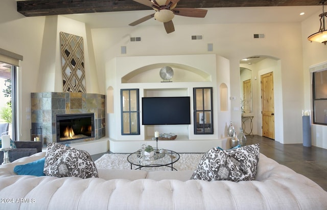 living room featuring beam ceiling, a fireplace, ceiling fan, and a high ceiling