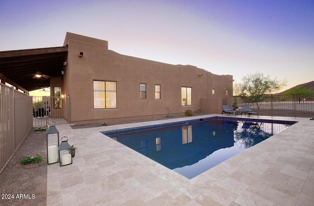 pool at dusk with ceiling fan and a patio area