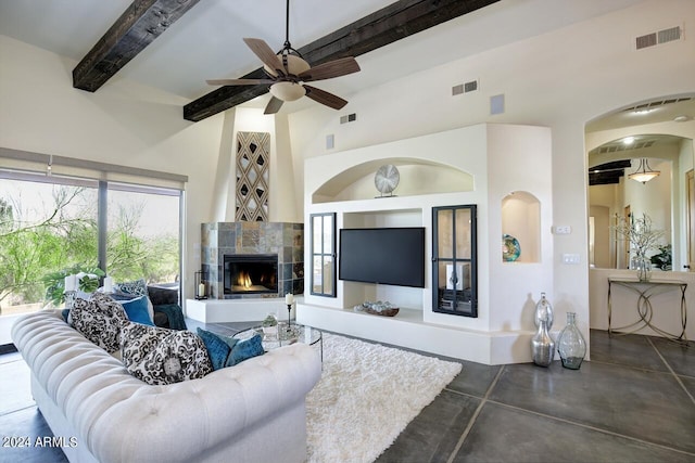 living room with a tiled fireplace, beam ceiling, and ceiling fan