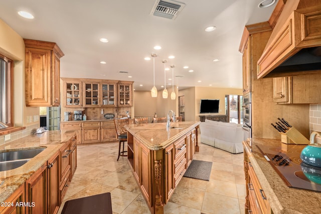 kitchen with an island with sink, backsplash, a kitchen bar, light stone countertops, and decorative light fixtures