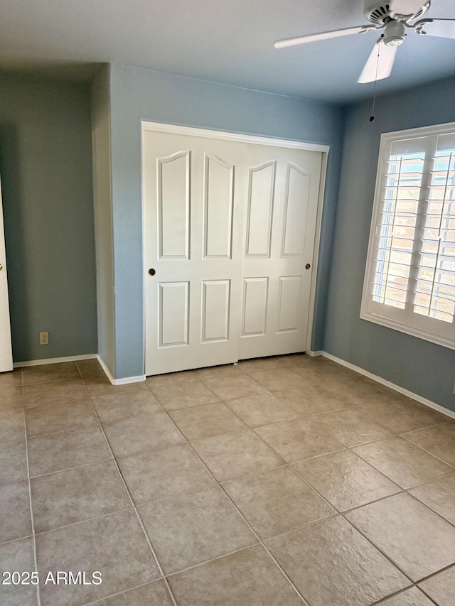 unfurnished bedroom featuring light tile patterned floors, a closet, baseboards, and a ceiling fan