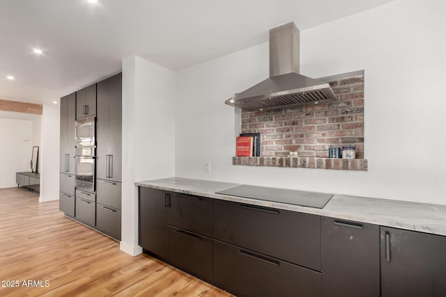 kitchen with island exhaust hood, appliances with stainless steel finishes, light stone counters, and light wood-type flooring