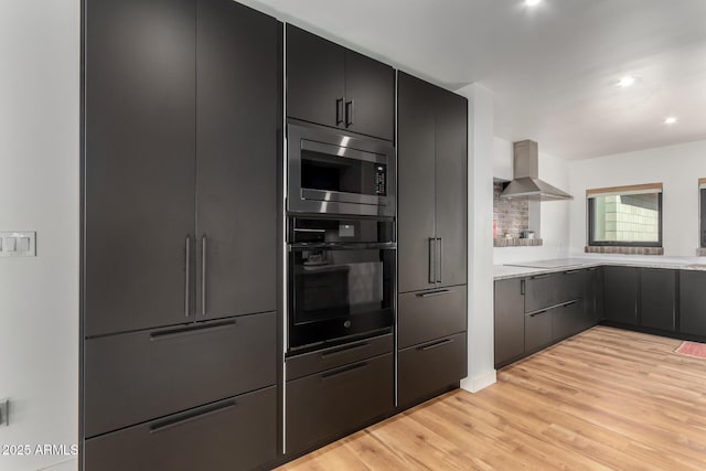 kitchen featuring tasteful backsplash, light hardwood / wood-style flooring, wall chimney range hood, and black appliances