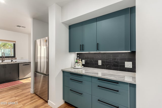 kitchen featuring light stone counters, appliances with stainless steel finishes, blue cabinets, and light wood-type flooring