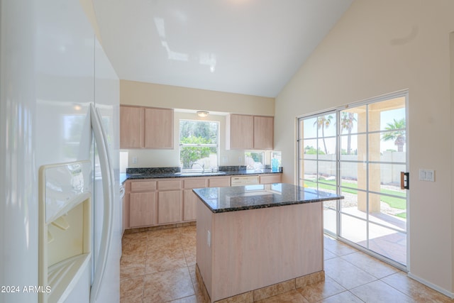 kitchen featuring white fridge, light brown cabinetry, a kitchen island, and dark stone counters