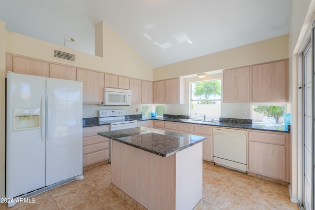 kitchen with light brown cabinetry, white appliances, a center island, and dark stone counters