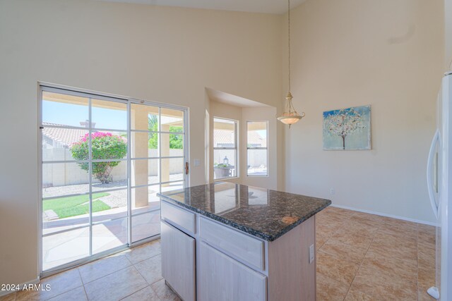 kitchen featuring light tile floors, a kitchen island, a high ceiling, dark stone countertops, and pendant lighting