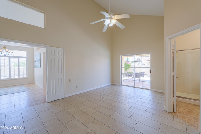 empty room with ceiling fan with notable chandelier, high vaulted ceiling, and light tile floors