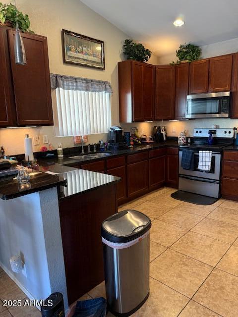 kitchen featuring a peninsula, dark countertops, a sink, appliances with stainless steel finishes, and vaulted ceiling
