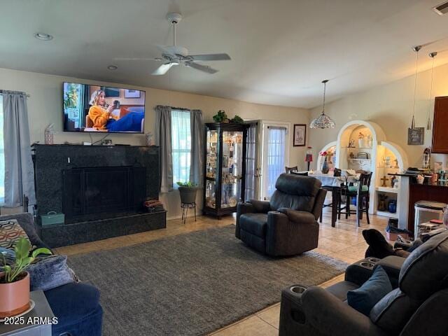 living room with a high end fireplace, a ceiling fan, light tile patterned floors, and a healthy amount of sunlight