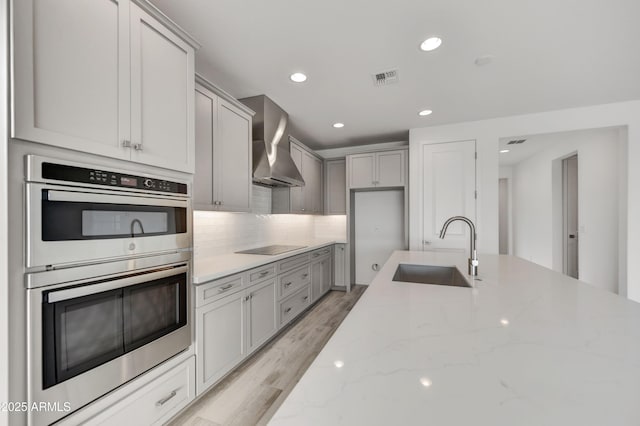 4128 Desert Moon Dr, Wickenburg, AZ 85390 - kitchen featuring stainless steel double oven, wall chimney range hood, a sink, light wood finished floors, and light stone counters