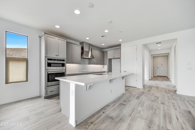 4128 Desert Moon Dr, Wickenburg, AZ 85390 - kitchen with wall chimney range hood, a sink, gray cabinets, double oven, and a center island with sink