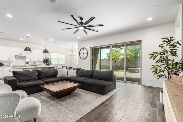 living room with ceiling fan with notable chandelier, dark wood-type flooring, and sink