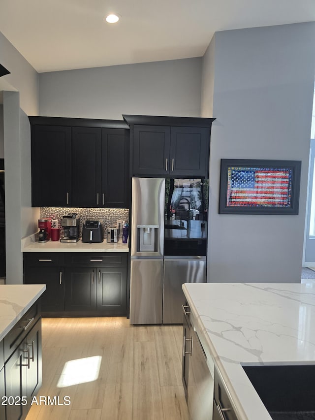 kitchen with stainless steel fridge with ice dispenser, backsplash, light hardwood / wood-style floors, and light stone countertops