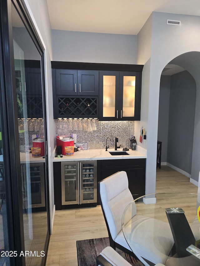 bar with wine cooler, sink, decorative backsplash, and light hardwood / wood-style flooring