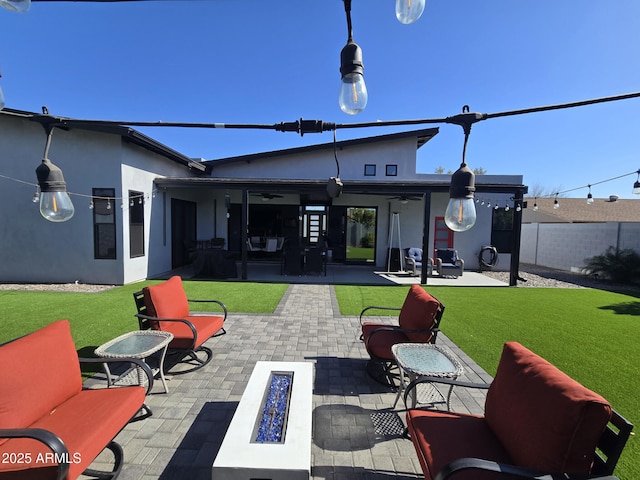 rear view of property featuring ceiling fan, an outdoor fire pit, a patio, and a lawn