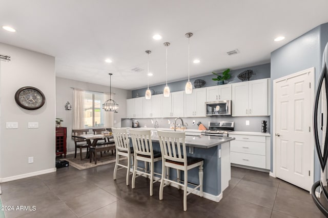 kitchen featuring hanging light fixtures, a center island with sink, white cabinetry, stainless steel appliances, and an inviting chandelier