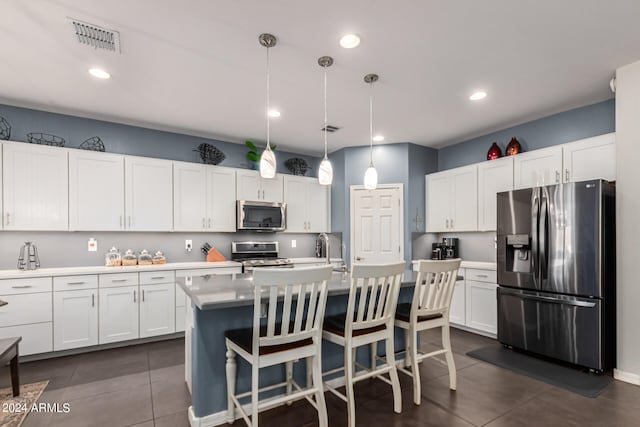 kitchen with pendant lighting, an island with sink, white cabinets, stainless steel appliances, and a kitchen bar