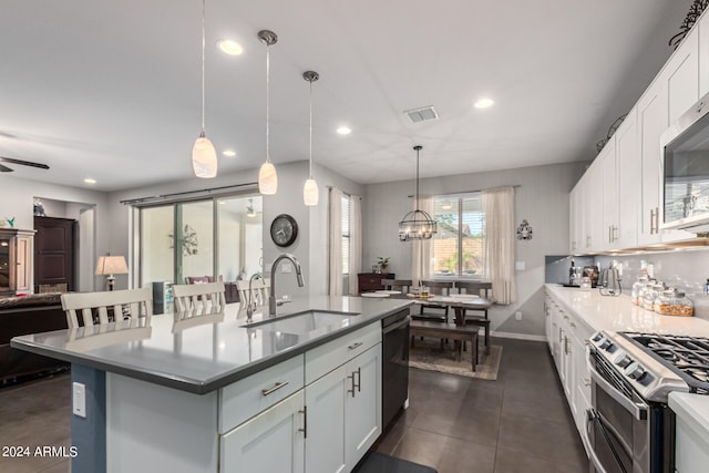 kitchen featuring a kitchen island with sink, sink, white cabinets, hanging light fixtures, and appliances with stainless steel finishes