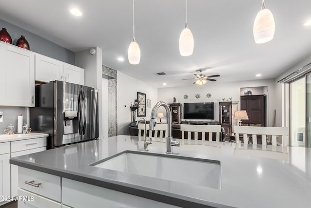 kitchen with stainless steel fridge, white cabinets, ceiling fan, decorative light fixtures, and sink