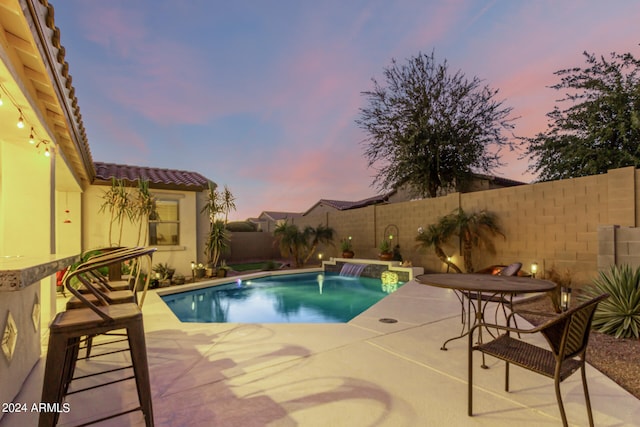 pool at dusk with pool water feature and a patio area