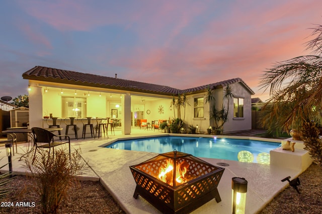 pool at dusk featuring a fire pit, a bar, and a patio area