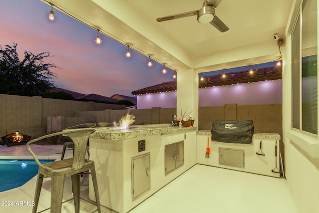 patio terrace at dusk featuring ceiling fan, grilling area, and a bar