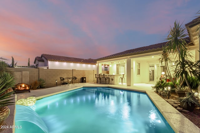 pool at dusk featuring a patio and an outdoor bar