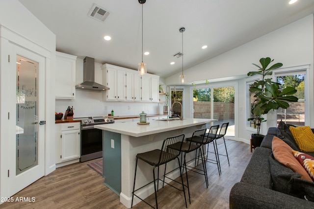 kitchen featuring pendant lighting, wall chimney range hood, sink, stainless steel range with electric stovetop, and white cabinets