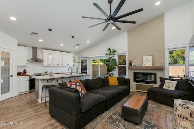 living room featuring sink, high vaulted ceiling, ceiling fan, a fireplace, and light hardwood / wood-style floors