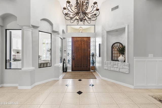 entrance foyer featuring a high ceiling, a chandelier, light tile patterned flooring, and decorative columns