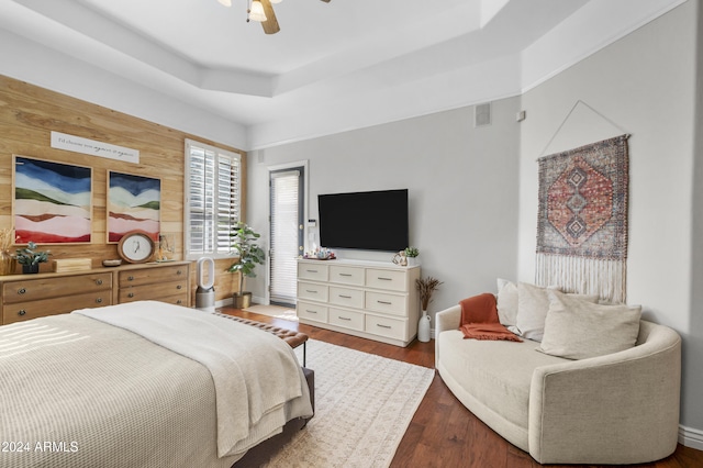 bedroom with dark wood-type flooring, a tray ceiling, wooden walls, and ceiling fan