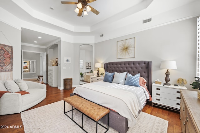 bedroom with dark wood-type flooring, ceiling fan, and a tray ceiling