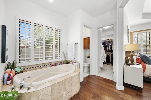 bathroom with tiled bath, wood-type flooring, a healthy amount of sunlight, and toilet