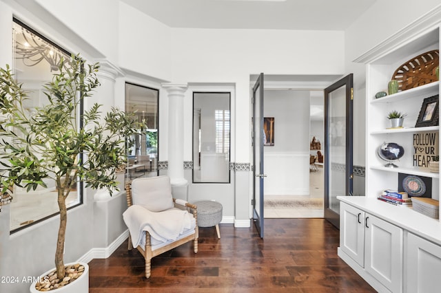 sitting room with dark wood-type flooring and decorative columns