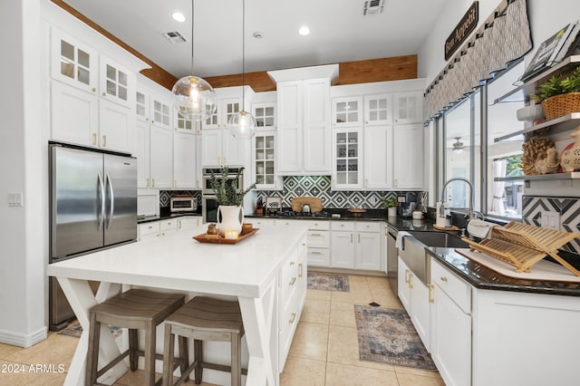 kitchen with stainless steel appliances, white cabinetry, light tile patterned floors, backsplash, and a center island