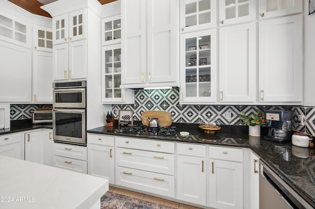 kitchen with dark stone countertops, white cabinetry, appliances with stainless steel finishes, and backsplash