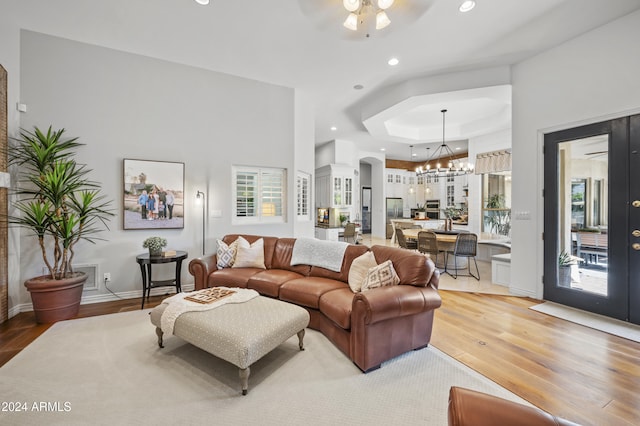 living room featuring wood-type flooring, a raised ceiling, and ceiling fan with notable chandelier