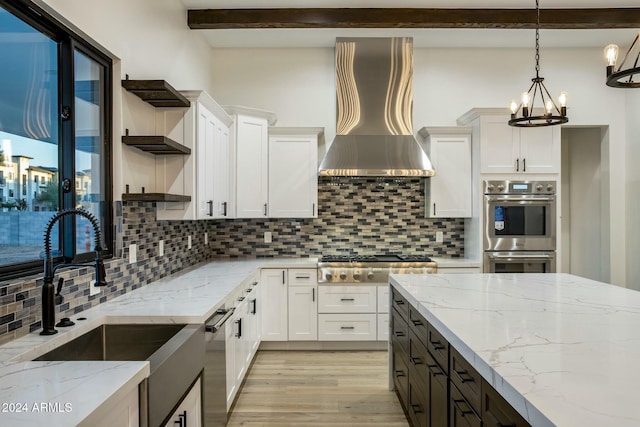 kitchen featuring appliances with stainless steel finishes, white cabinets, hanging light fixtures, light stone counters, and wall chimney exhaust hood