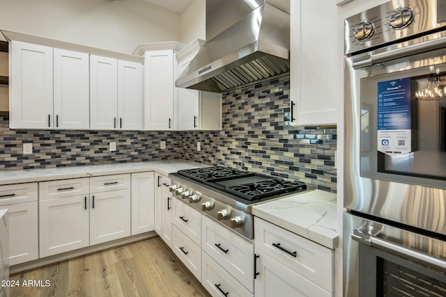 kitchen with white cabinetry, wall chimney range hood, stainless steel appliances, and tasteful backsplash