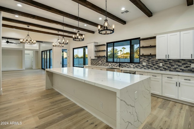 kitchen with pendant lighting, white cabinets, light stone counters, and a spacious island