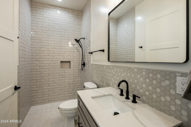 bathroom with a tile shower, vanity, tile walls, and toilet