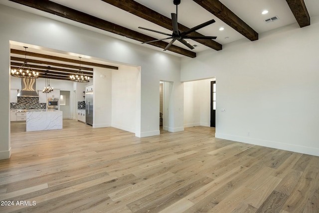 unfurnished living room with ceiling fan with notable chandelier, light hardwood / wood-style flooring, and beamed ceiling