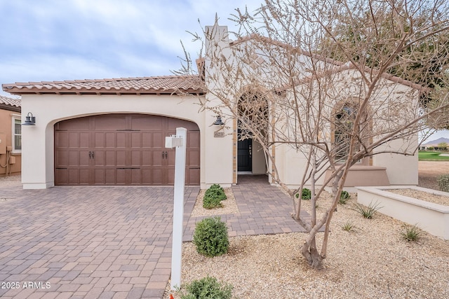 mediterranean / spanish-style home featuring a tiled roof, decorative driveway, an attached garage, and stucco siding