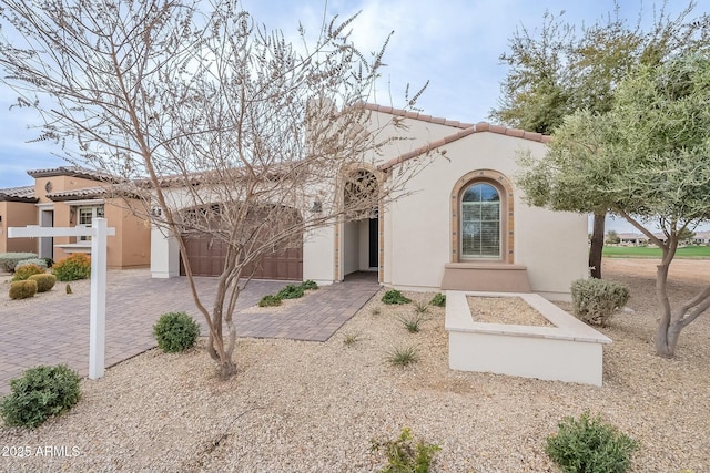 mediterranean / spanish home with stucco siding, an attached garage, a tile roof, and decorative driveway