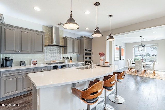 kitchen featuring a sink, decorative backsplash, wall chimney range hood, and gray cabinetry