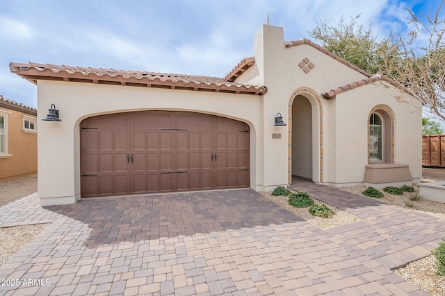 mediterranean / spanish-style home featuring stucco siding, an attached garage, a tile roof, and decorative driveway