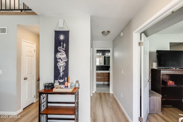 hallway with baseboards, wood finished floors, and visible vents